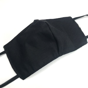 May include: A solid black fabric face mask featuring a contoured center seam for a structured fit. The mask includes thin black elastic ear loops attached to each side, providing a simple and functional design for covering the nose and mouth area.