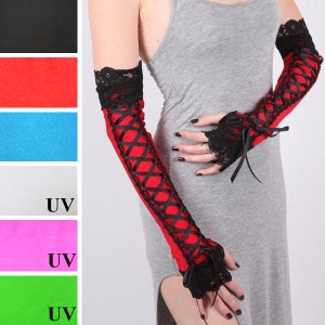 May include: Red and black arm warmers with a lace and ribbon design. The arm warmers feature black lace cuffs and a crisscross ribbon pattern. These gothic-style arm warmers are a unique accessory.