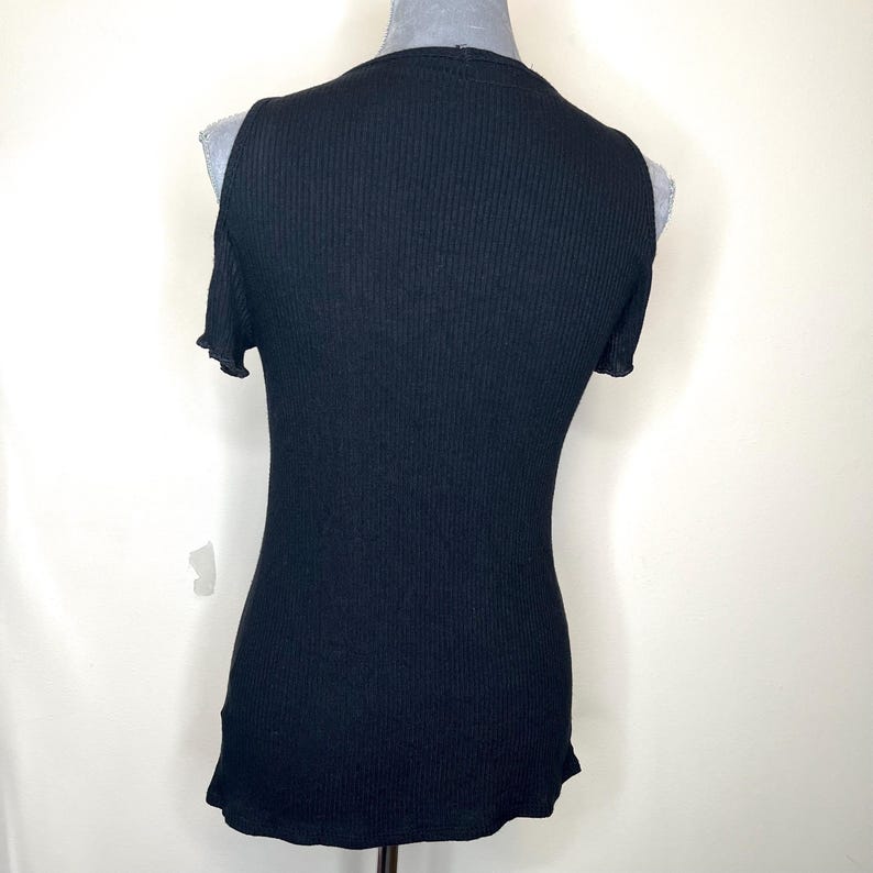 May include: Black ribbed knit top with cold shoulder cutouts. The sleeveless shirt has a scoop neck and a fitted silhouette. The fabric has vertical ribbing. The top is displayed on a mannequin.