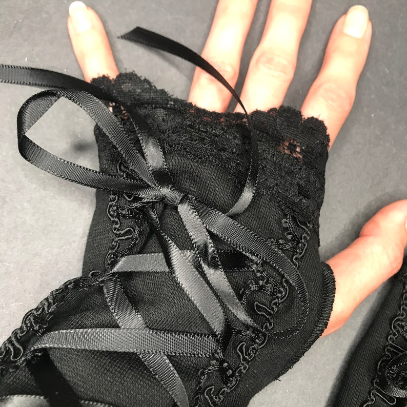 May include: Black lace fingerless gloves with a satin ribbon tie. The gloves have a delicate lace trim and are tied at the wrist with a black satin ribbon.
