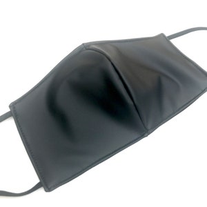 May include: A solid black face mask featuring a smooth, matte finish with a central vertical seam for structure. The mask includes matching black elastic ear loops attached to the sides, providing a clean, uniform appearance across the entire surface.