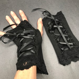 May include: A pair of black fingerless gloves with lace trim and black ribbon lacing. The gloves are tied with a bow at the wrist.