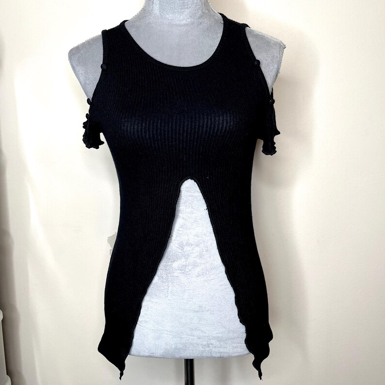 May include: Black ribbed knit top with a unique split front design. The sleeveless top features a round neckline and small shoulder cutouts. The top is displayed on a mannequin.