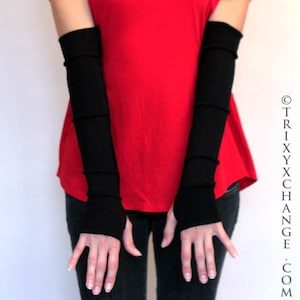 May include: A pair of black fingerless arm warmers made of a soft, stretchy fabric. The arm warmers are worn by a person wearing a red shirt and black pants.