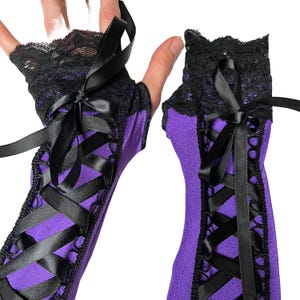 May include: A pair of purple fingerless gloves with black lace trim and black satin ribbon accents. The gloves feature a crisscross ribbon design and a bow at the wrist. The gloves are made of a soft, stretchy material.