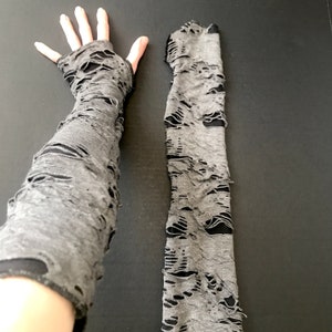 May include: A pair of gray distressed arm warmers. The arm warmers are made of a soft, stretchy fabric and have a lot of holes in them. They are perfect for adding a touch of edge to any outfit.