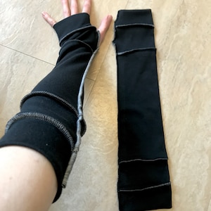 May include: A pair of black arm warmers with a gray seam detail. The arm warmers are made of a soft, stretchy fabric and are perfect for keeping your arms warm in the cooler months.