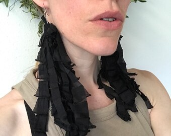 May include: A pair of long black tassel earrings with a layered, ruffled design.
