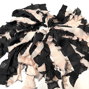 May include: Close-up of a handmade accessory featuring layered fabric strips in black and pale pink. The strips are ruffled and create a textured, decorative effect. The accessory appears to be a scarf or collar.