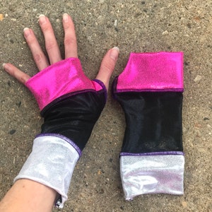 May include: A pair of black and pink fingerless gloves with white trim. The gloves have a pink and black design on the top and a white trim on the bottom.