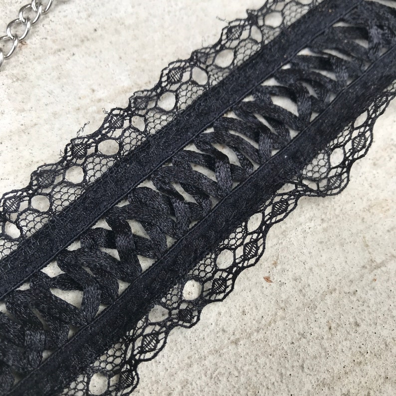 May include: Black lace trim with a woven design. The lace has a scalloped edge.