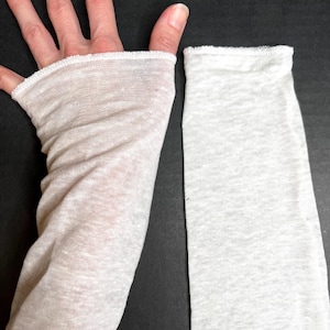 May include: A light beige fingerless glove and a matching sleeve, both made of a sheer, lightweight fabric. The glove has a thumb hole and covers the hand up to the knuckles. The sleeve is long and straight, with a finished edge.