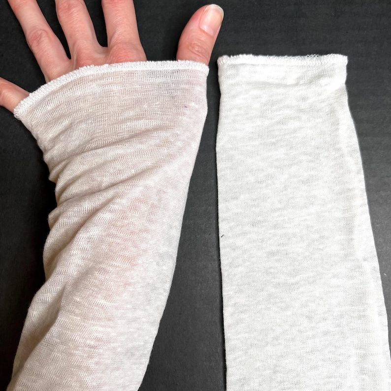 May include: A light beige fingerless glove and a matching sleeve, both made of a sheer, lightweight fabric. The glove has a thumb hole and covers the hand up to the knuckles. The sleeve is long and straight, with a finished edge.