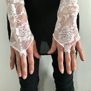 May include: A pair of white lace fingerless gloves with a floral pattern. The gloves have a delicate, feminine look and are perfect for adding a touch of elegance to any outfit.
