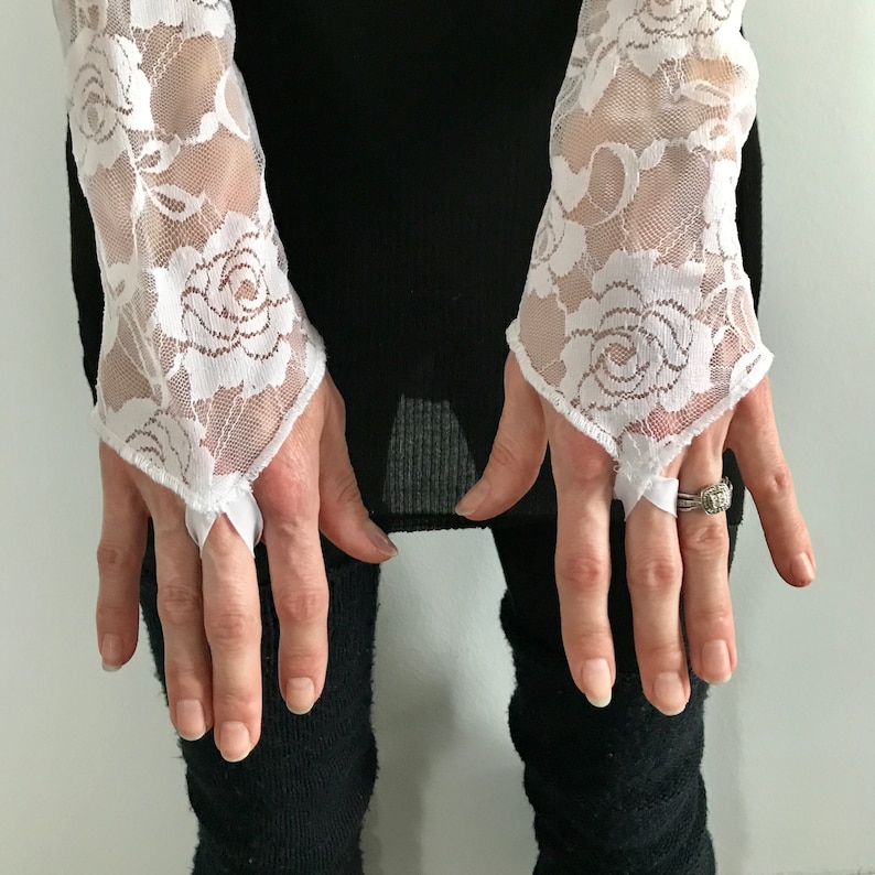 May include: A pair of white lace fingerless gloves with a floral pattern. The gloves have a delicate, feminine look and are perfect for adding a touch of elegance to any outfit.