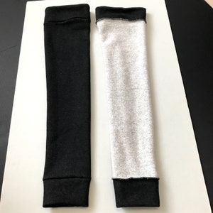 Puede incluir: Dos calentadores de brazo. Uno es negro liso, el otro es gris jaspeado. Ambos tienen un pu&ntilde;o negro en la parte superior e inferior. Los calentadores de brazo est&aacute;n hechos de un material suave y el&aacute;stico.
