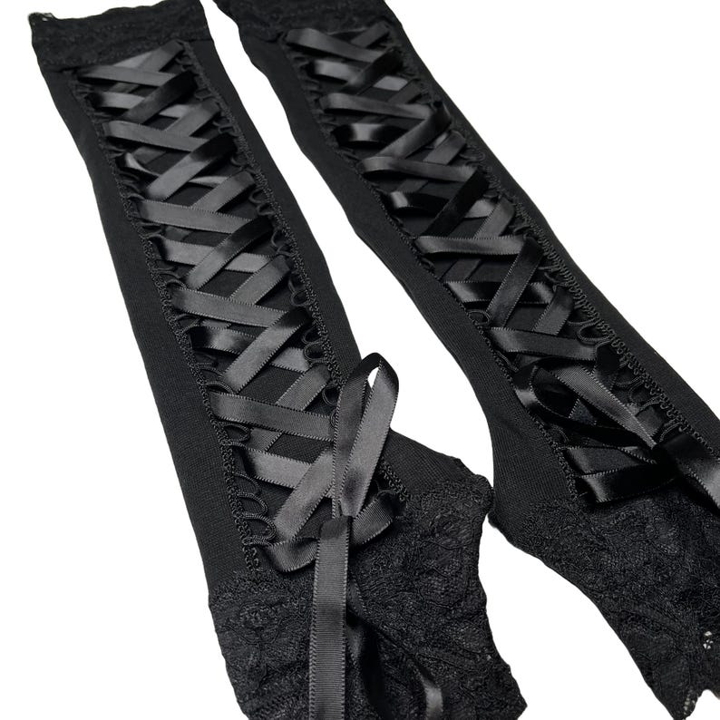 May include: A pair of black fingerless gloves featuring a long, vertical lace-up design with satin ribbon threaded through eyelets. The gloves are finished with intricate black lace trim at the wrist and a decorative ribbon bow at the base.