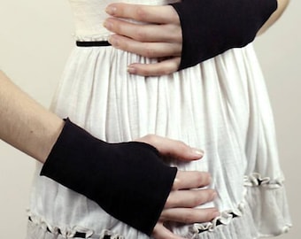 May include: A pair of solid black fingerless gloves made of a smooth fabric, covering the back of the hands and wrists, paired with a white sleeveless top featuring a gathered waist and a ruffled hemline with thin black trim accents.