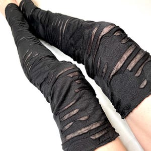 May include: Black leg warmers with a distressed, ripped look. The fabric is thin and has a mesh-like appearance.