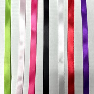 May include: Seven vertical strips of smooth satin ribbon arranged side by side in a spectrum of colors including lime green, pale pink, hot pink, black, white, bright red, and deep purple, each featuring a consistent sheen and texture.