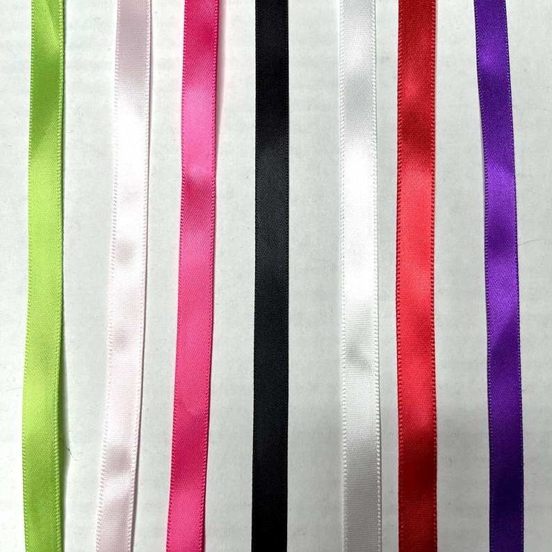 May include: Seven vertical strips of smooth satin ribbon arranged side by side in a spectrum of colors including lime green, pale pink, hot pink, black, white, bright red, and deep purple, each featuring a consistent sheen and texture.