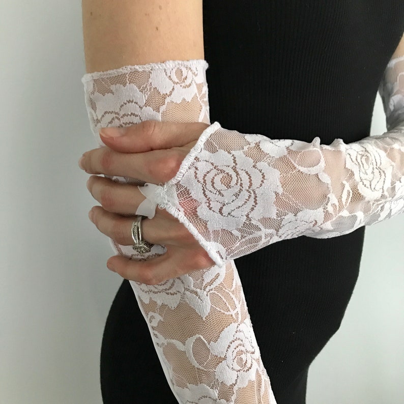 May include: White lace elbow length gloves with a floral pattern. The gloves are made of a sheer fabric and have a delicate, feminine look.