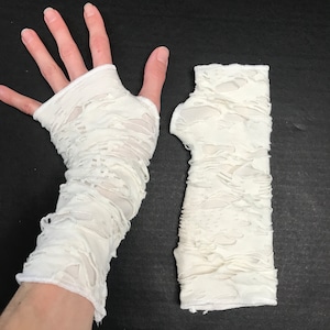 May include: A pair of white fingerless gloves with a distressed, ripped look. The gloves are made of a soft, stretchy fabric.