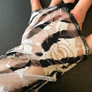 May include: Black and white lace fabric with a floral pattern. The fabric is sheer and has a delicate texture.
