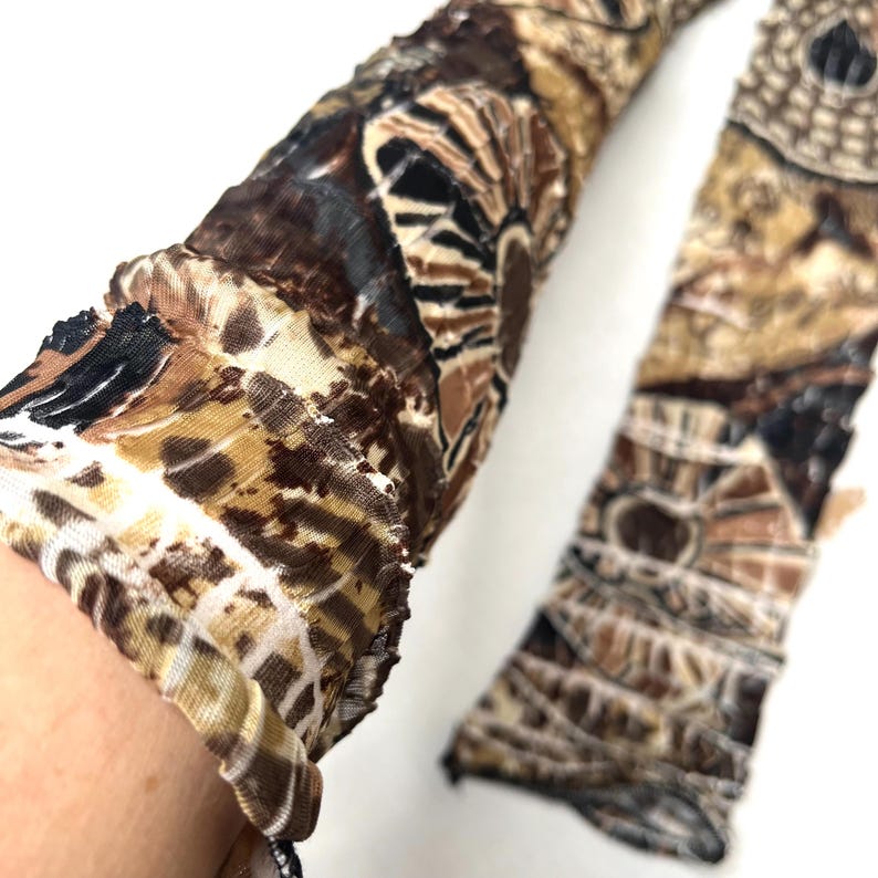 May include: A pair of long, sheer, crinkled fabric sleeves featuring a brown, black, and cream abstract geometric pattern. The material has a textured, pleated appearance with a semi-transparent quality, extending down the length of the arm.