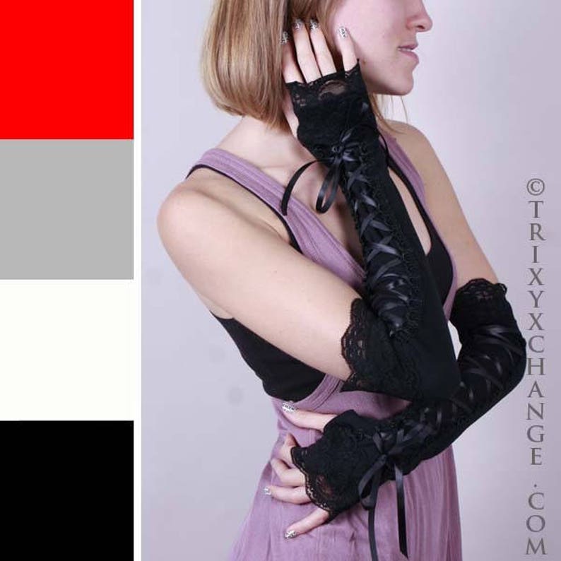 May include: A pair of black lace fingerless gloves with ribbon ties. The gloves are long and extend past the elbows. The gloves are worn by a person with short blonde hair.