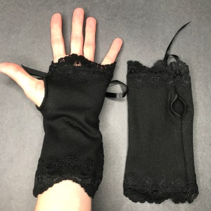 May include: A pair of black fingerless gloves with lace trim and a black ribbon. The gloves are made of a soft, stretchy fabric.