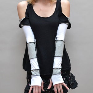 May include: A black sleeveless top with a white and gray striped arm warmers. The arm warmers have a black trim and are worn over the top of the sleeves.