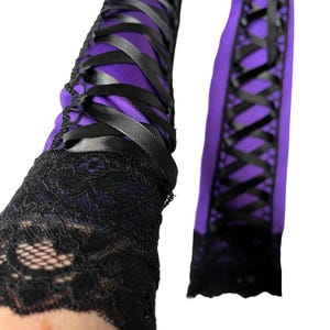 May include: Purple and black arm warmers with a lace cuff. The arm warmers feature a purple fabric base, crisscrossed with black satin ribbons. The cuffs are made of black lace.