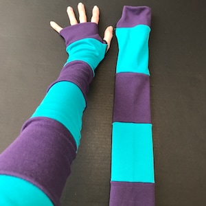 May include: A pair of striped arm warmers in teal and purple. One arm warmer is on a hand, and the other is lying flat.
