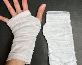 May include: A pair of white fingerless gloves made from a sheer, lightweight mesh fabric. The gloves feature a series of horizontal, gathered ruffles that create a textured, layered appearance. One glove is worn on a hand, while the other lies flat.