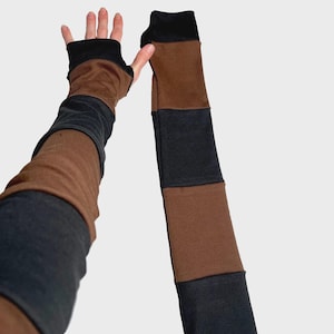 May include: Arm warmers in shades of brown, black, and gray. The fingerless gloves have a black cuff and a brown and gray color block design. The long sleeves are made of a soft material.