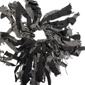 Könnte beinhalten: Ein handgefertigtes Scrunchie mit einem einzigartigen Design mit ausgefransten Kanten. Das Scrunchie besteht aus schwarzen und grauen Stoffstreifen, die einen strukturierten, geschichteten Effekt erzeugen. Das Scrunchie ist für einen Pferdeschwanz oder Dutt konzipiert.