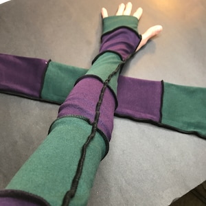 May include: A pair of long arm warmers made from a patchwork of green and purple fabric with black stitching. The arm warmers are fingerless and have a stretchy fit.