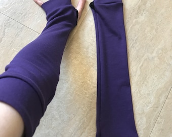 May include: A pair of long, solid purple arm warmers featuring thumb holes. One arm warmer is worn on an arm, while the other lies flat. The fabric is a smooth, opaque material with a consistent deep purple color throughout both pieces.