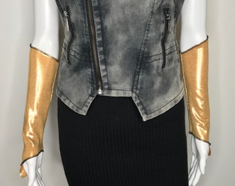 May include: A pair of gold metallic fingerless gloves with a black trim. The gloves are worn on a mannequin wearing a black skirt and a gray denim vest.