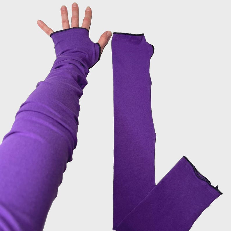 May include: A pair of long, solid purple arm warmers made of a smooth, stretchy fabric. Each arm warmer features a thumb hole and a simple black stitched trim along the edges, extending from the fingers up to the upper arm area for full coverage.