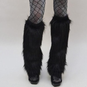 May include: A pair of black faux fur leg warmers worn over silver glittery fishnet tights and black platform shoes. The leg warmers feature long, shaggy black synthetic fibres that extend from the mid-calf down to the top of the footwear.
