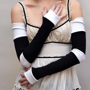 May include: Black and white arm warmers. The arm warmers are black with white cuffs at the wrist and upper arm. The arm warmers are long and cover the arms from the wrist to the upper arm.