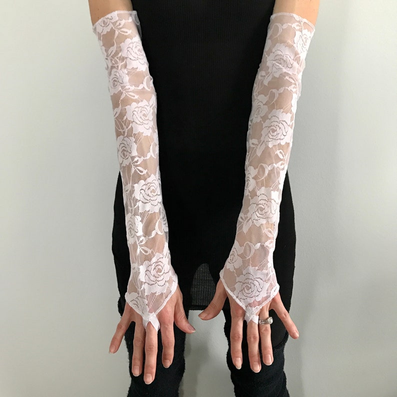 May include: A pair of white lace fingerless gloves with floral designs. The gloves are made of a sheer, delicate fabric and have a fitted style.