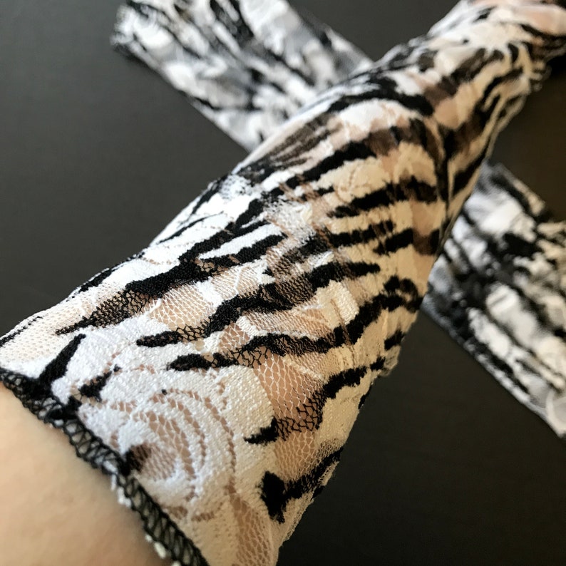 May include: Black and white lace gloves with a zebra print pattern. The gloves are made of a sheer fabric and have a delicate floral design.