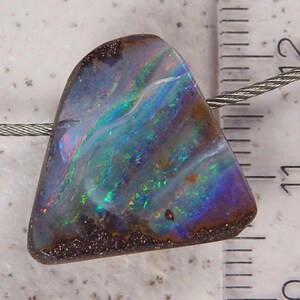 May include: A blue, green, and purple opal pendant with a dark brown backing. The pendant is hanging from a silver chain and is approximately 1.1 inches in length.