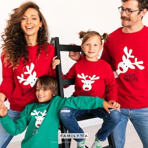 May include: A family wearing matching red and green Christmas sweaters with a white reindeer graphic. The sweaters have the text "#Team Rudolph" and "#Team". The family is smiling and posing for a photo.