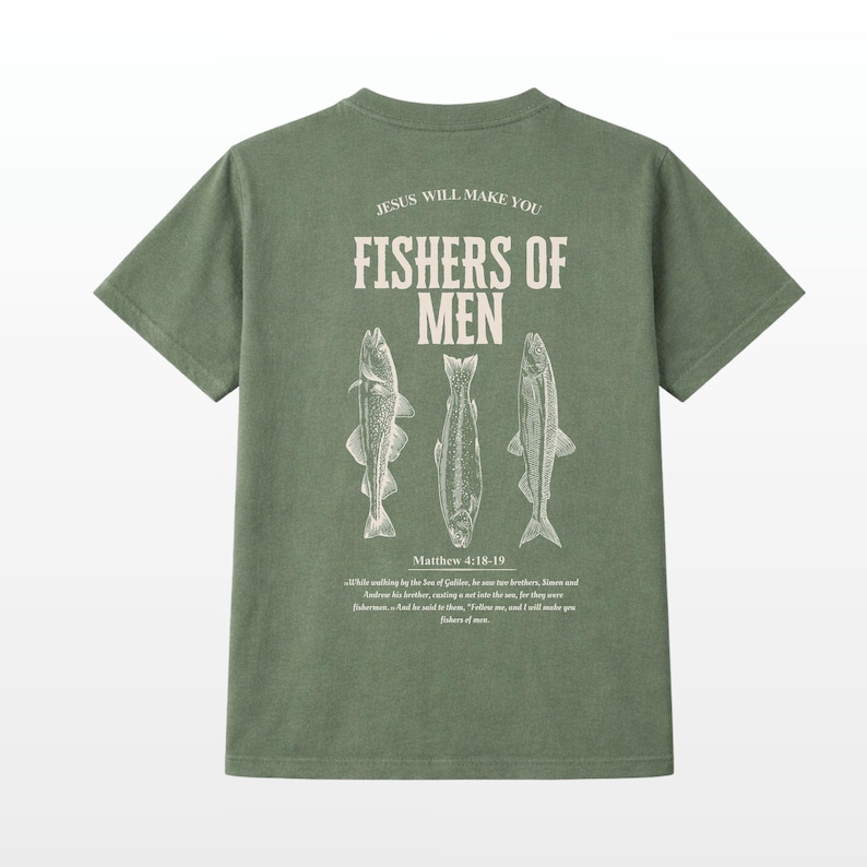 Puede incluir: Camiseta verde oliva con el texto "JESUS WILL MAKE YOU FISHERS OF MEN" y tres ilustraciones de peces. El texto "Matthew 4:18-19" y un vers&iacute;culo b&iacute;blico est&aacute;n impresos debajo.