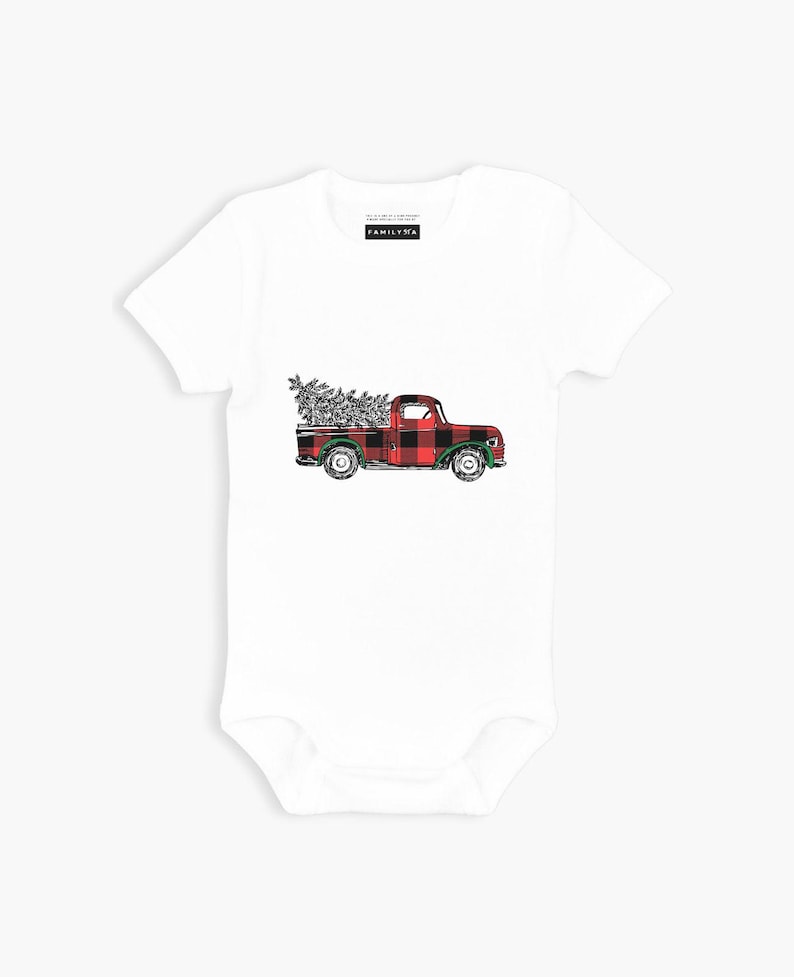 May include: White baby bodysuit with a red and black plaid pickup truck carrying a Christmas tree. The truck has green wheels and a white background.