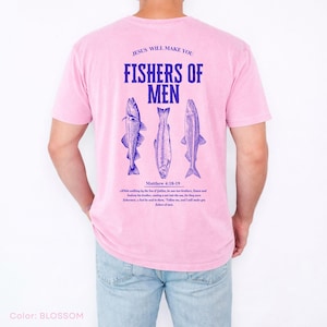 Puede incluir: Camiseta rosa claro con el texto azul "JESUS WILL MAKE YOU FISHERS OF MEN" y tres ilustraciones de peces azules. El texto "Matthew 4:18-19" tambi&eacute;n est&aacute; impreso. La camiseta es de color pastel claro.